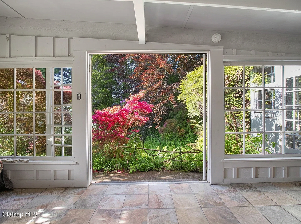 Empty sunroom with garden doors opening to mature rhododendrons and azaleas